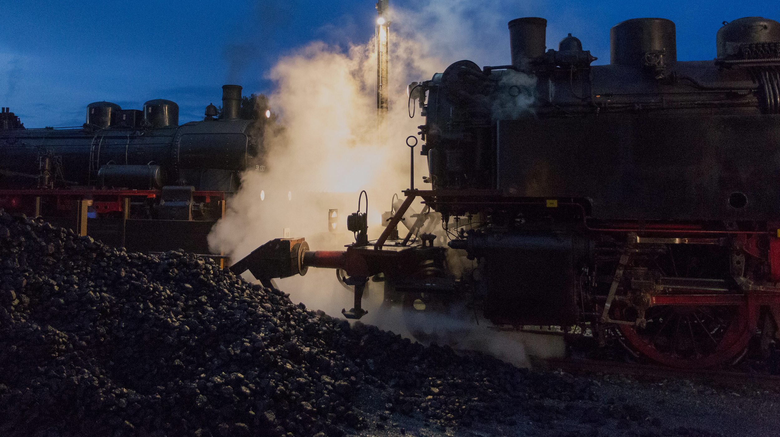 Two steam locomotives and a pile of coal at night